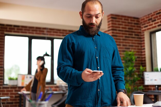 Empresario sosteniendo un teléfono inteligente moderno esperando una llamada importante mirando el tiempo del reloj mientras trabaja en la presentación del negocio en la oficina de startuo. Gerente ejecutivo analizando documentos de estrategia de marketing