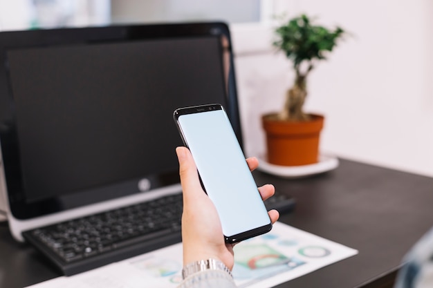 Empresario sosteniendo teléfono inteligente con pantalla en blanco contra el escritorio