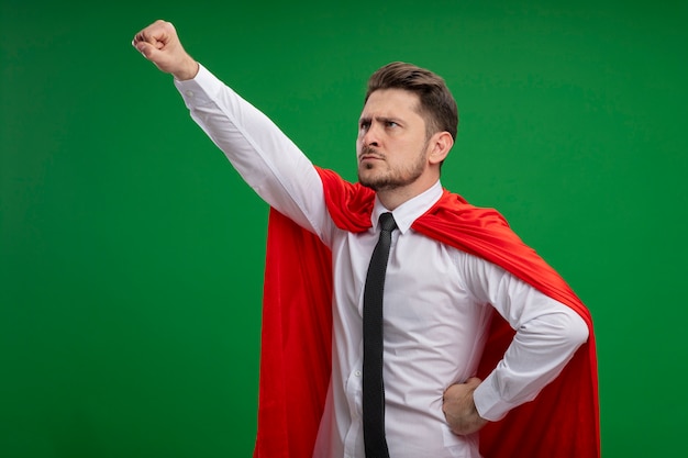 Empresario de superhéroe en capa roja sosteniendo la corona manteniendo el brazo en gesto de vuelo listo para luchar de pie sobre fondo verde