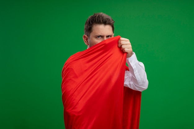 Foto gratuita empresario de superhéroe envuelto con capa roja mirando a la cámara con rostro serio de pie sobre fondo verde