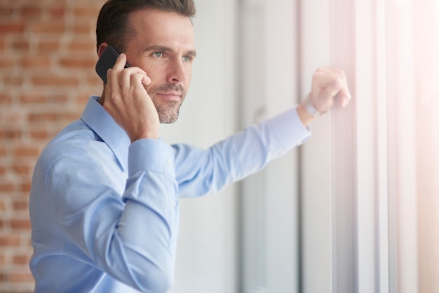 Empresario con teléfono apoyado en la ventana