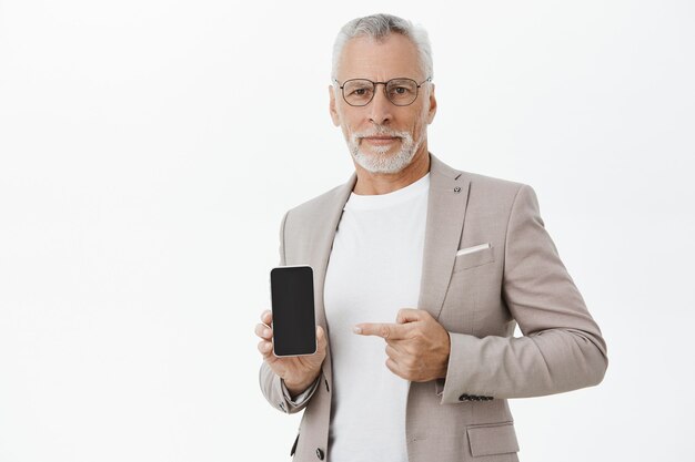 Empresario de traje y gafas apuntando con el dedo a la pantalla del teléfono móvil