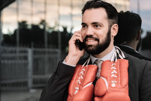 Empresario en un traje hablando por su teléfono móvil con guantes de boxeo rojos colgando de su cuello apoyado