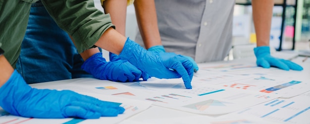 Los empresarios de Asia discutiendo una reunión de lluvia de ideas de negocios juntos comparten datos, usando mascarilla y guantes en el trabajo en la nueva oficina normal. Estilo de vida y distanciamiento social después del coronavirus.