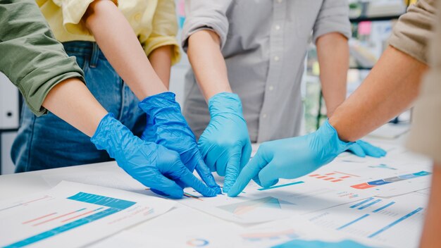 Los empresarios de Asia discutiendo una reunión de lluvia de ideas de negocios juntos comparten datos, usando mascarilla y guantes en el trabajo en la nueva oficina normal. Estilo de vida y distanciamiento social después del coronavirus.