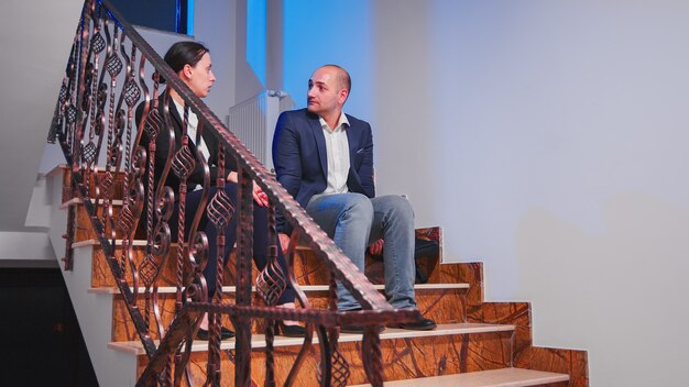 Empresarios cansados con exceso de trabajo tomando un descanso sentado en las escaleras en la oficina de negocios corporativos discutiendo. Colega empresario haciendo horas extraordinarias juntos a altas horas de la noche haciendo planes para el proyecto de fecha límite