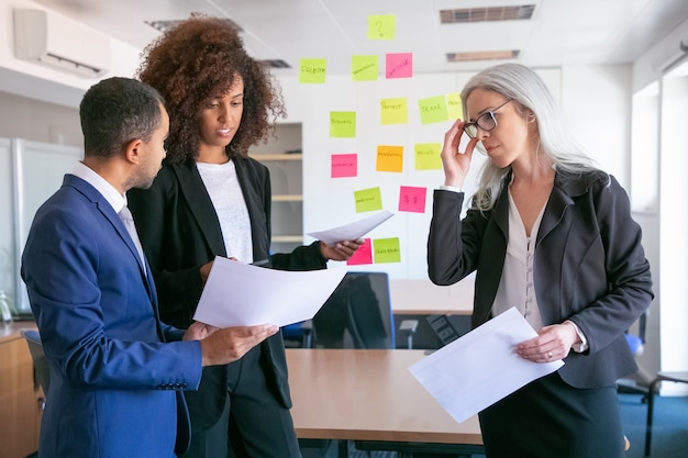 Empresarios confiados discutiendo datos analíticos. Gerentes experimentados exitosos en trajes de oficina reunidos en sala de conferencias y estrategia de planificación. Concepto de trabajo en equipo, negocios y gestión