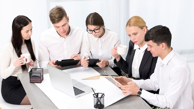 Empresarios creativos con móvil; Computadora portátil y tableta digital trabajando juntos en la oficina.
