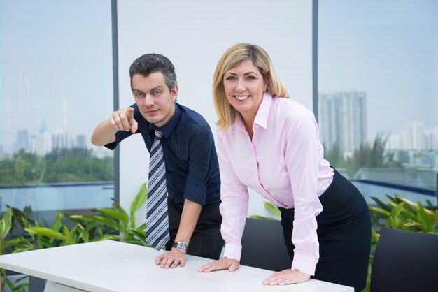 Empresarios emprendedores positivos apoyándose en la mesa y mirando a la cámara