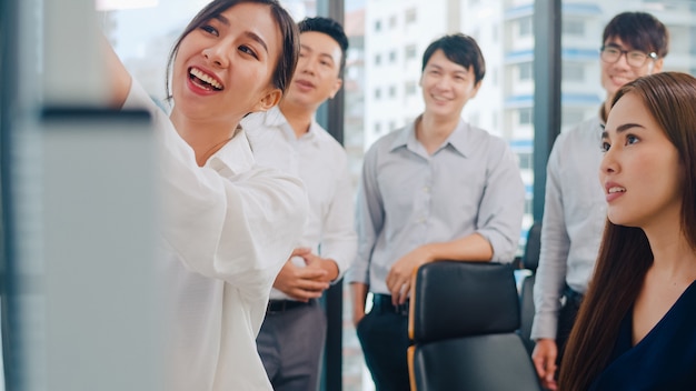 Empresarios y empresarias de Asia que se reúnen ideas de lluvia de ideas que conducen a colegas del proyecto de presentación comercial que trabajan juntos planean la estrategia de éxito disfrutan del trabajo en equipo en una pequeña oficina moderna.