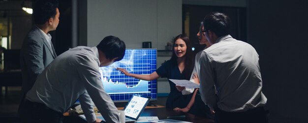 Empresarios y empresarias de Asia que se reúnen ideas de lluvia de ideas que conducen a colegas del proyecto de presentación de negocios que trabajan juntos planean la estrategia de éxito disfrutan del trabajo en equipo en una pequeña oficina nocturna moderna