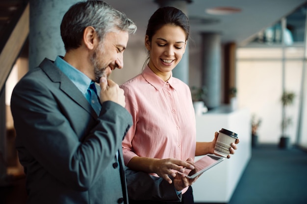 Empresarios felices cooperando mientras usan el panel táctil en un pasillo