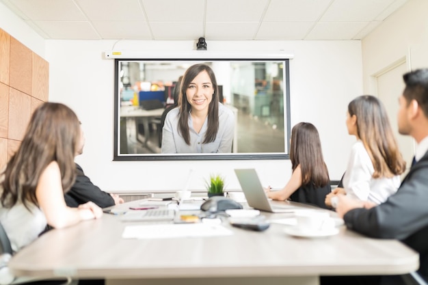 Empresarios multiétnicos mirando la pantalla de proyección en blanco mientras se sientan en la mesa de conferencias en la oficina