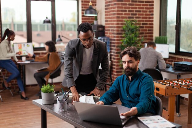 Empresarios multiétnicos que intercambian ideas para proyectos de marketing mientras trabajan en la estrategia de la empresa en la oficina de inicio de la pared de ladrillo. Equipo diverso que analiza estadísticas que planifican la colaboración empresarial