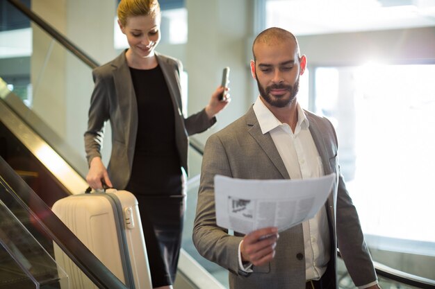 Empresarios de pie en escaleras mecánicas con equipaje