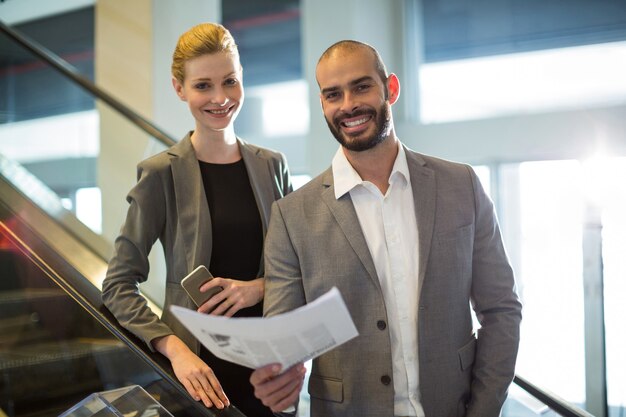 Empresarios de pie en escaleras mecánicas con equipaje