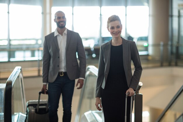 Empresarios sonrientes con equipaje de pie delante de una escalera mecánica