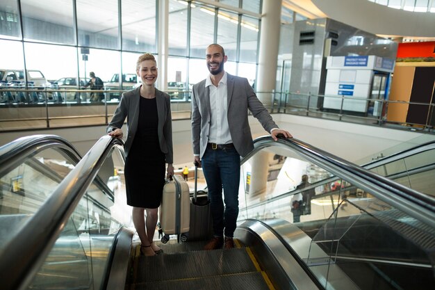 Empresarios sonrientes con equipaje subiendo escaleras mecánicas