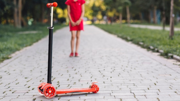 Foto gratuita empuje el scooter frente a la niña de pie en la pasarela del parque