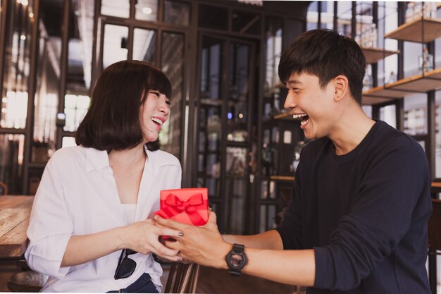 Enamorados sonriendo mientras la chica sujeta un regalo rojo