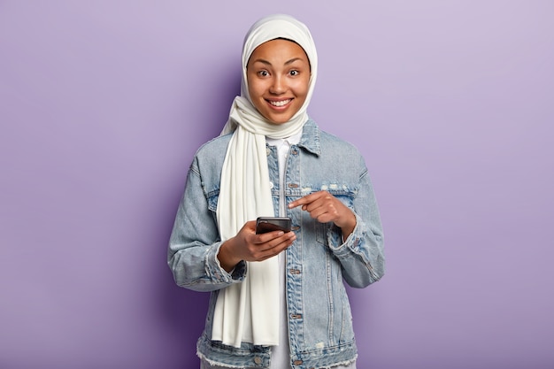 encantada joven musulmana posando con su teléfono