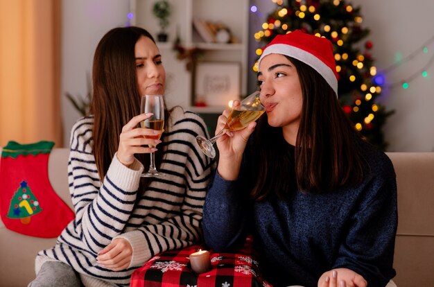 Encantado de chicas guapas bebiendo copas de champán sentados en sillones y disfrutando de la Navidad en casa