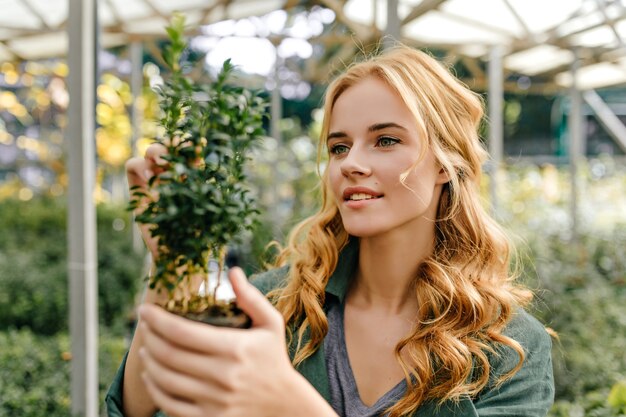 Encantado, el explorador estudia la estructura de la planta. Mujer joven en top verde lindo sonriendo posando para el retrato.