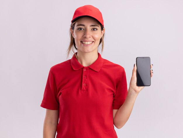 Encantado de joven bonita repartidora en uniforme sostiene teléfono en blanco