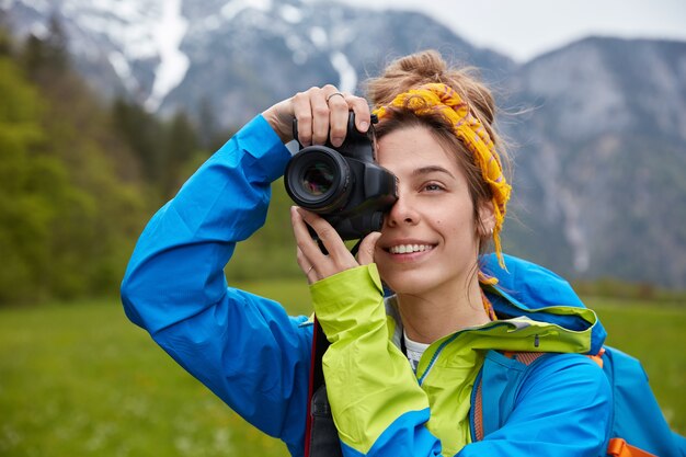 Encantado de joven europea toma una foto durante el viaje de senderismo, sostiene una cámara profesional