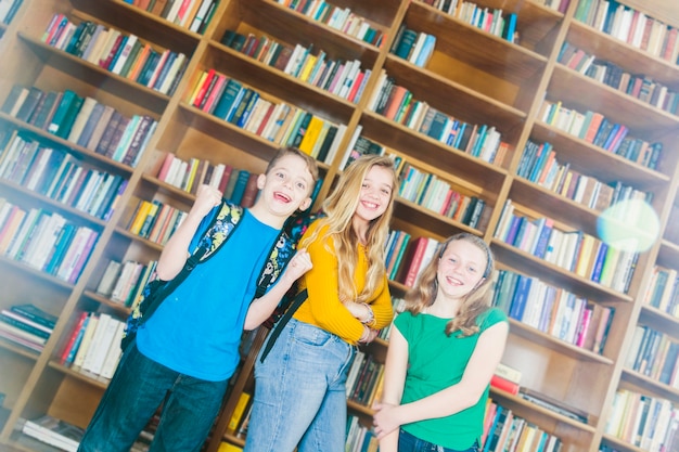 Encantado de niños sonrientes de pie en la biblioteca de la escuela