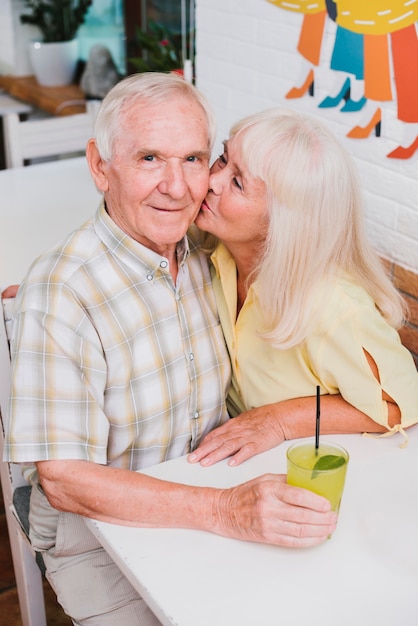 Foto gratuita encantado pareja de ancianos besándose en la cafetería y disfrutando de una bebida refrescante