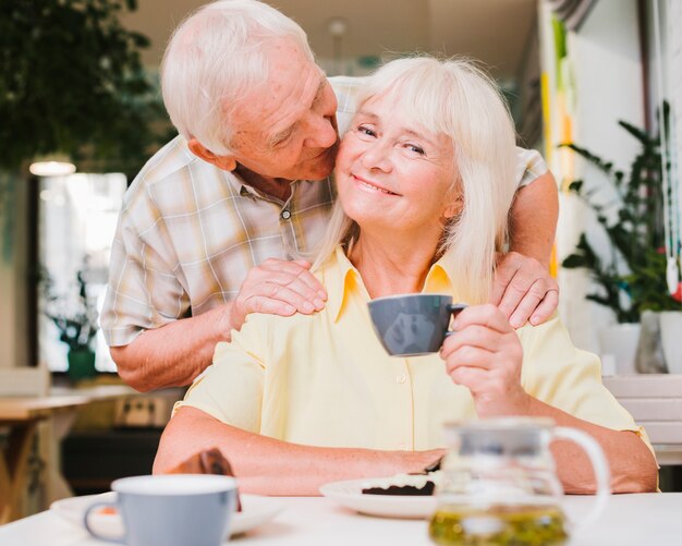 Encantado pareja de ancianos sentados en la cafetería y besos