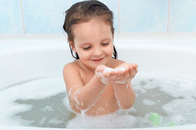 Encantador bebé feliz tomando baño, jugando con burbujas de espuma felizmente.