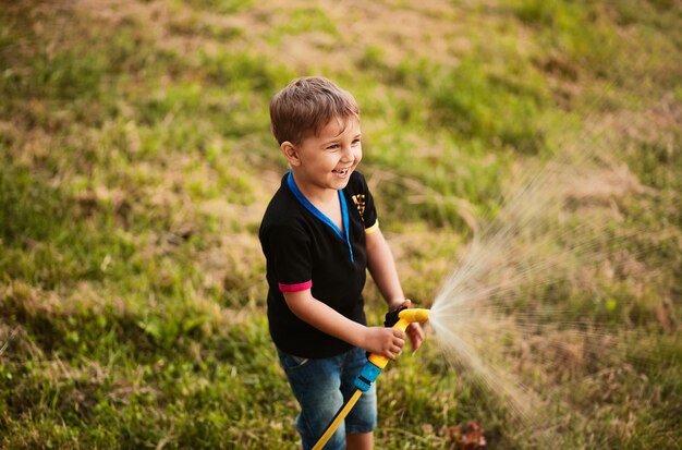 Encantador niño aguas verde hierba en el patio trasero