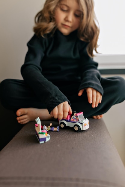 Encantadora adorable niña bonita con peinado ondulado está jugando con juguetes en casa Adorable niña está jugando con autos Juegos creativos para niños que se quedan en casa durante el encierro