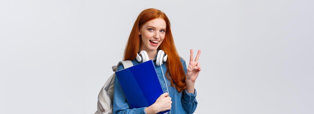 Encantadora y amigable estudiante universitaria pelirroja con documentos en papel para la escuela con mochila y w