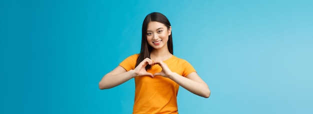 Foto gratuita encantadora cariñosa atractiva novia asiática muestra el signo del corazón aprecia y valora la relación hermano sonriente