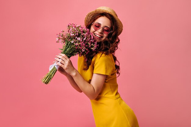 Encantadora chica en canotier y gafas de sol rojas posa con flores rosas