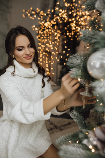 Encantadora chica está colgando un juguete en un árbol de Navidad