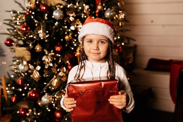 Foto gratuita encantadora chica europea sosteniendo regalos sobre el árbol de navidad en casa