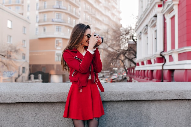 Encantadora chica en falda roja tomando fotografías de la ciudad de la primavera