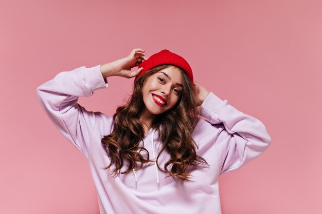 Encantadora chica fresca en sudadera con capucha morada se pone sombrero rojo