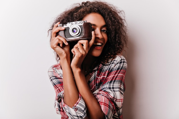 Encantadora chica negra tomando fotos con una sonrisa Foto interior de una dama africana despreocupada con cámara