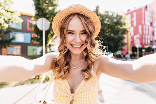 Encantadora chica pálida haciendo selfie en la ciudad. Foto al aire libre de mujer rubia alegre en traje amarillo divirtiéndose.