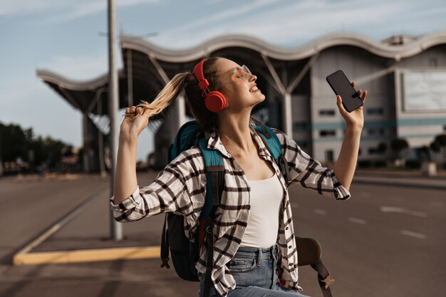 Encantadora chica rubia con gafas de sol, auriculares rojos escucha música