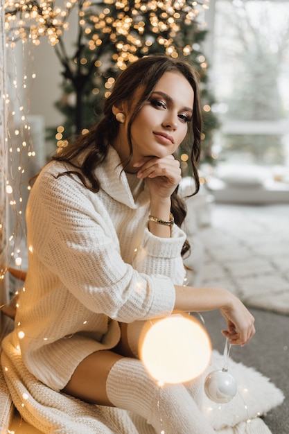 Encantadora chica con un vestido de punto sostiene un juguete de Navidad y tiene un aspecto de ensueño