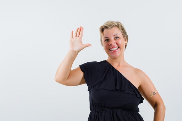 Encantadora dama de blusa negra agitando la mano para saludar y mirar alegre