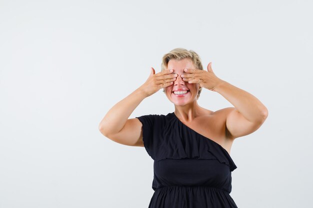 Encantadora dama en blusa negra cogidos de la mano en los ojos y luciendo optimista