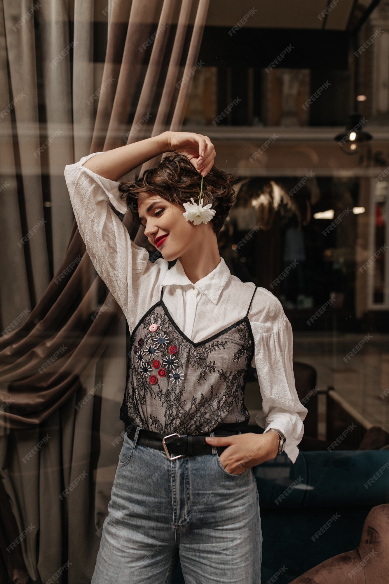 Encantadora dama camisa blanca con encaje negro y jeans sonriendo en la cafetería. mujer con labios brillantes pelo corto tiene flor dentro. | Foto Gratis