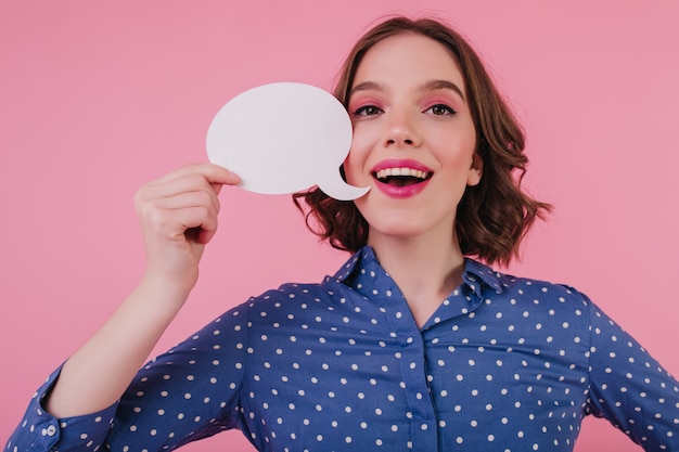 Encantadora dama caucásica con corte de pelo corto pensando en algo con una sonrisa. Chica blanca alegre con maquillaje rosa posando